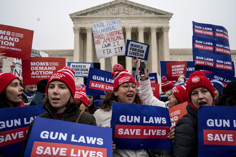 A crowd of people hold signs about gun laws in front of the U.S. Supreme Court building