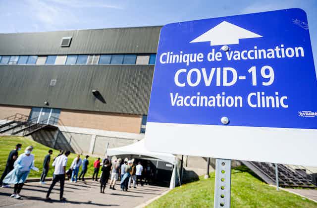People walking under a tent and into a building near a COVID-19 vaccination clinic sign