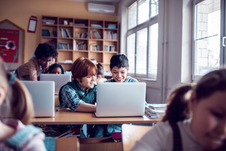 Two young boys at school share a class assignment on a laptop.