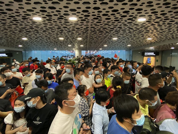 A crowd of people wearing masks gather in an airport arrival hall.