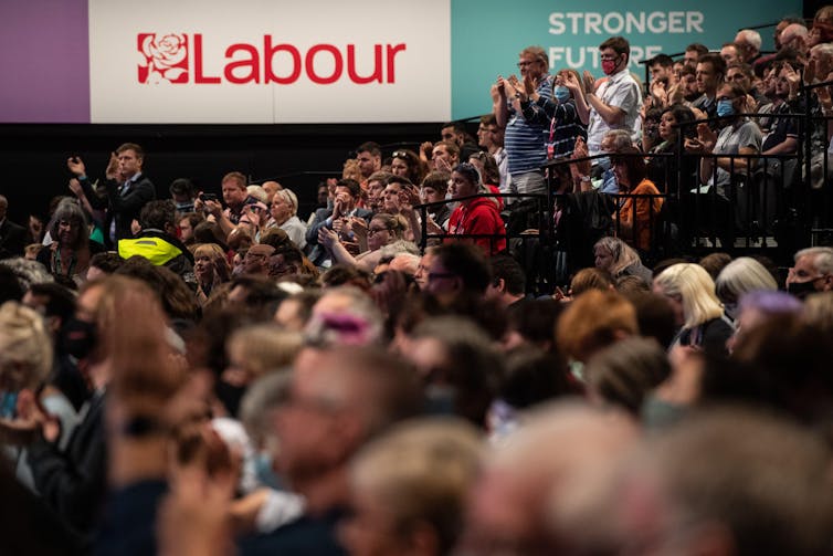 A large group of delegates standing in the Labour party conference main hall
