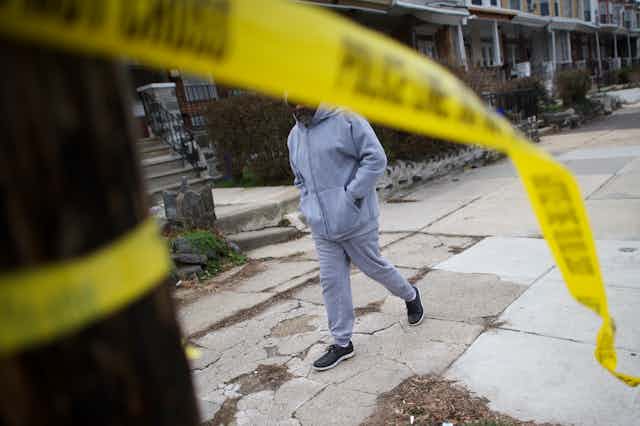 A man walks past a crime scene as police tape hangs from a tree in the foreground
