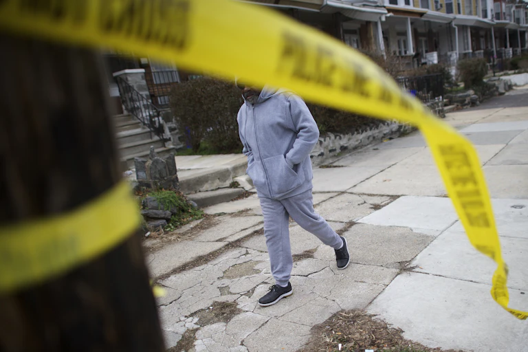 A man walks past a crime scene as police tape hangs from a tree in the foreground