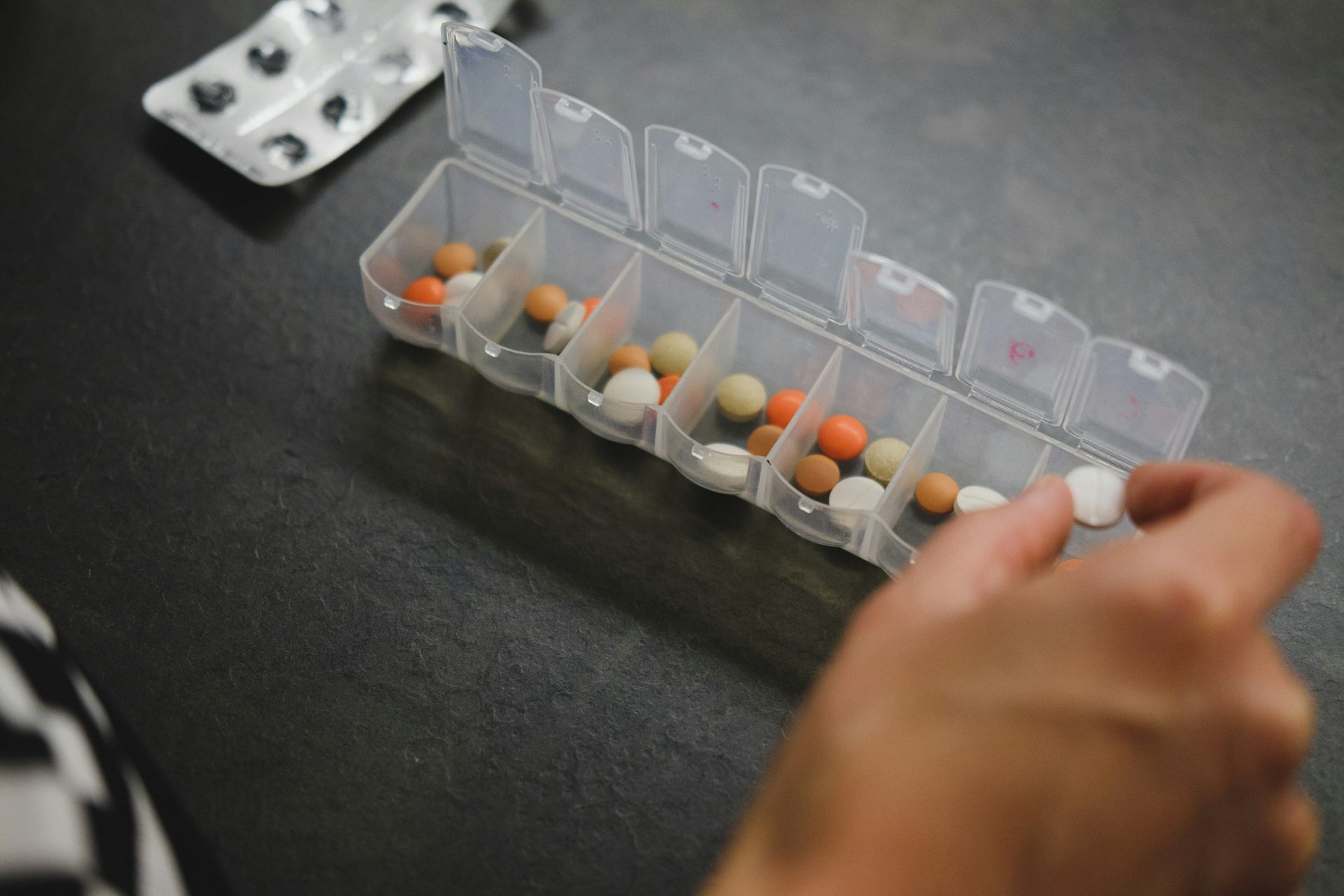 A person's hand taking a pill from a seven-days-a-week pill organizer.