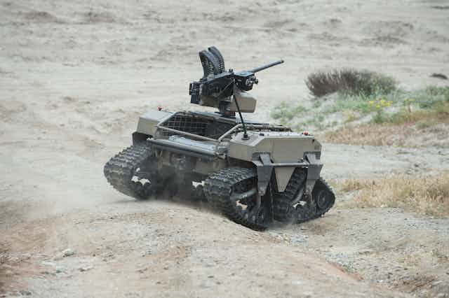 A small tracked vehicle with a machine gun mounted on top moves across a desert landscape