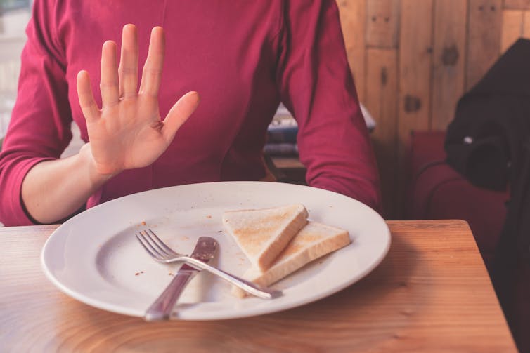 woman holds up hand in front of plate