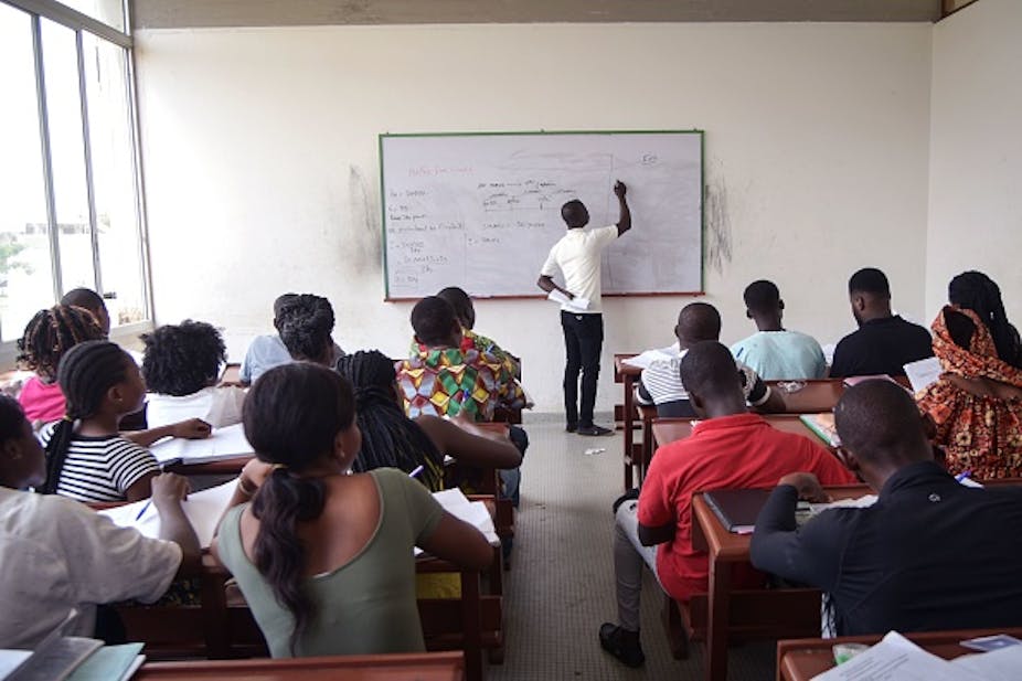 A teacher writing on a white board in a classroom filled with students.