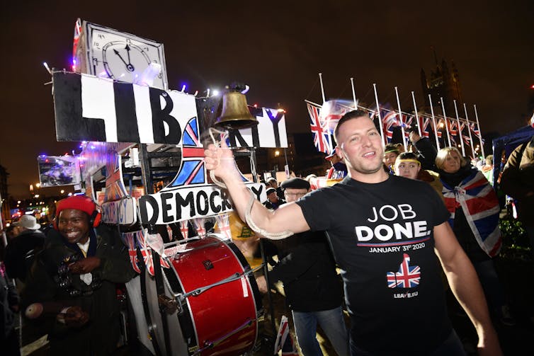 man in black t-shirt in front of pro-Brexit signs
