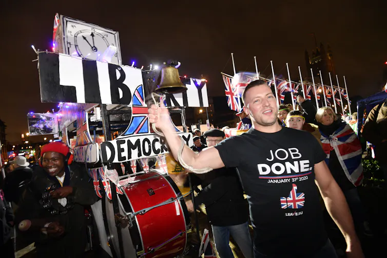 man in black t-shirt in front of pro-Brexit signs