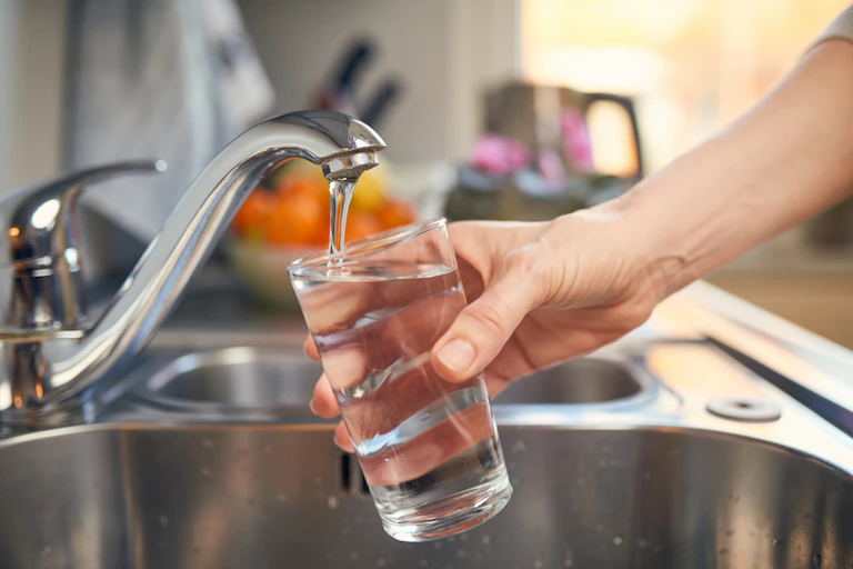 A person pouring a glass of water from the tap.