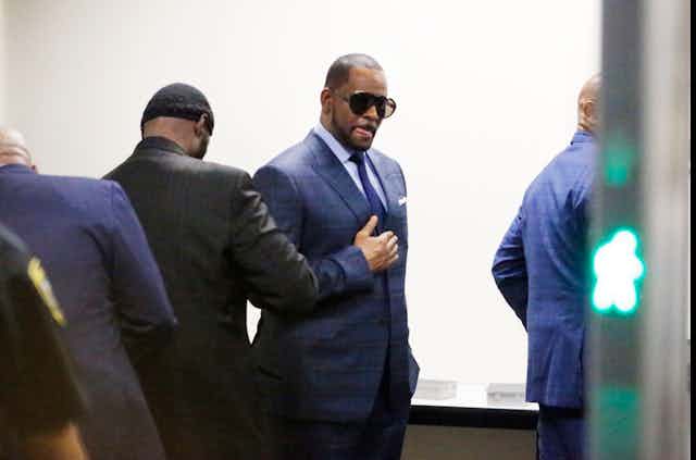 R. Kelly dressed in a suit and sunglasses walks through security checkpoint on the way to court.