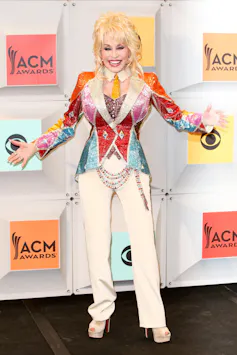 Dolly Parton wearing a colourful coat and white trousers.