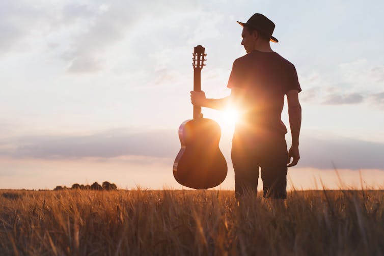 Silhouette of guitarist in field at sunset.