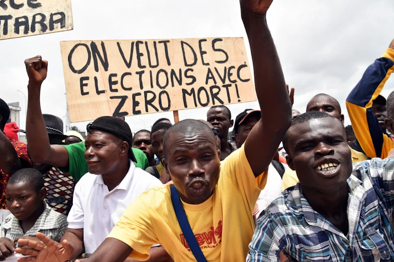 Foule avec pancarte sur laquelle il est écrit "on veut des élections avec zéro mort !"