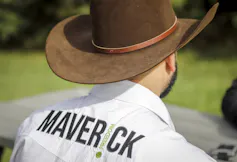 A man wearing a cowboy hat and a shirt that reads Maverick on the back is photographed from behind