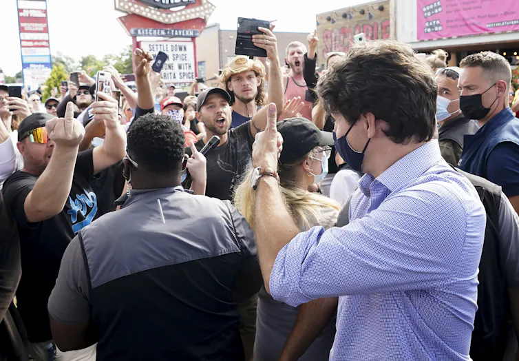 Justin Trudeau gives a thumbs up to protesters giving him the middle finger and shouting at him.