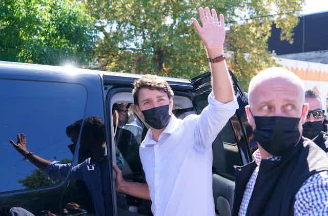 Justin Trudeau wearing a black surgical mask, waving as he enters an SUV