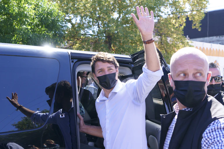 Justin Trudeau wearing a black surgical mask, waving as he enters an SUV