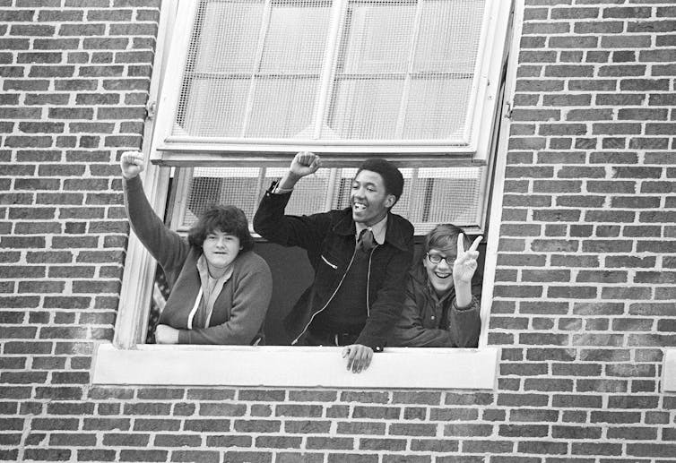 Several students wave and cheer through a window in a brick building