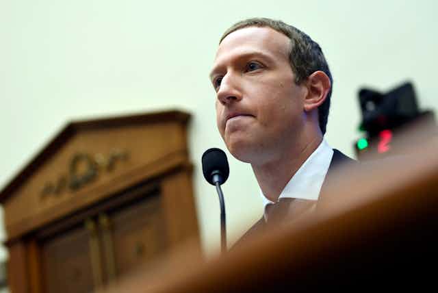 Mark Zuckerberg looks forward with a microphone by his mouth during testimony on Capitol Hill  