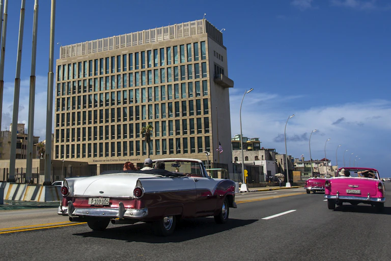 Classic cars driving past a tall cement building.