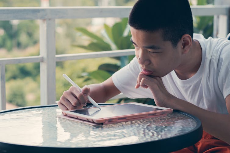 A disabled by sits at a table, drawing on an iPad with a digital pen.