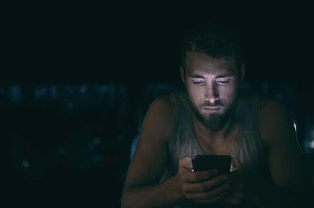 A man looks at his phone in the dark.