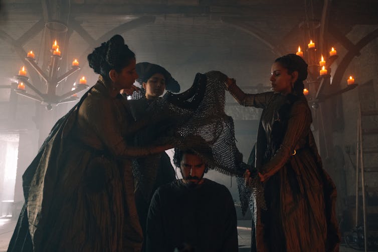 Dev Patel is getting dressed by three women.
