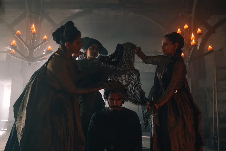 Dev Patel is getting dressed by three women.