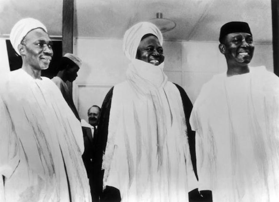 Three men standing and holding hands. The first two from the left are wearing head turbans.