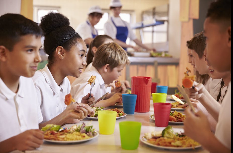 School children eating a nutritious lunch together in the cafeteria.