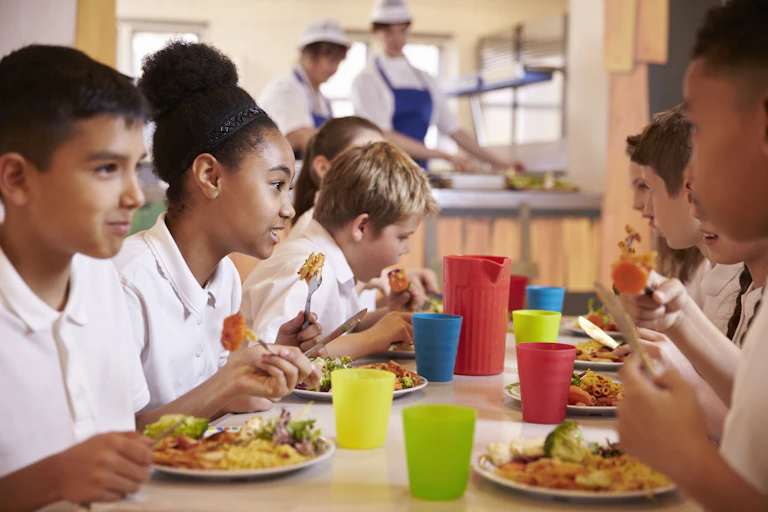 School children eating a nutritious lunch together in the cafeteria.