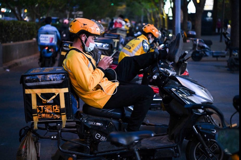 Delivery drivers sit on their electric scooters while waiting for orders outside a restaurant in Beijing, April 26, 2021. 