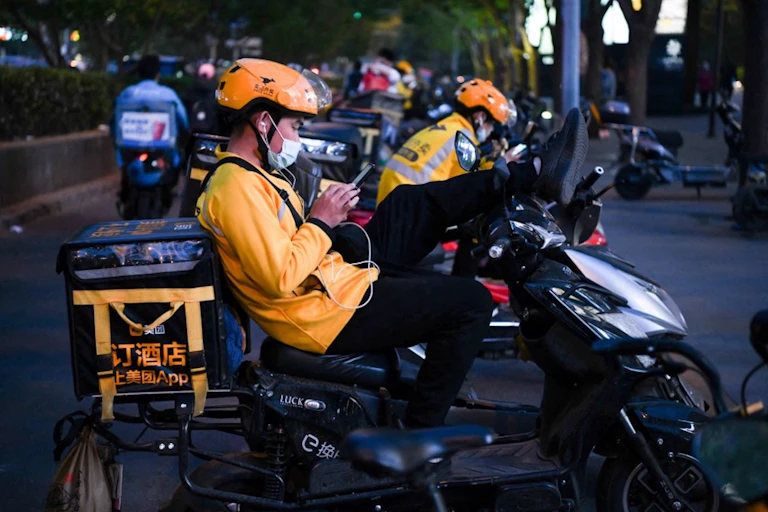 Delivery drivers sit on their electric scooters while waiting for orders outside a restaurant in Beijing, April 26, 2021.