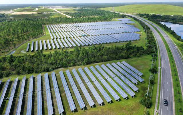 Fields of solar panels bounded by trees and a highway 