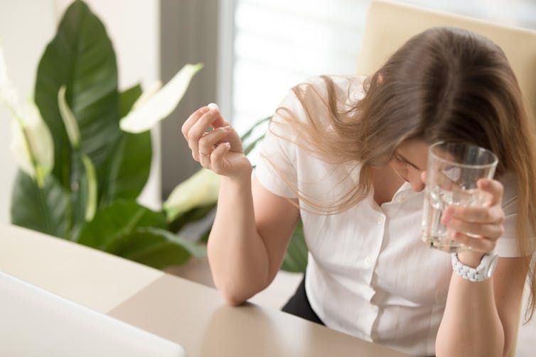 Une femme qui a mal à la tête prend un cachet avec son verre d’eau