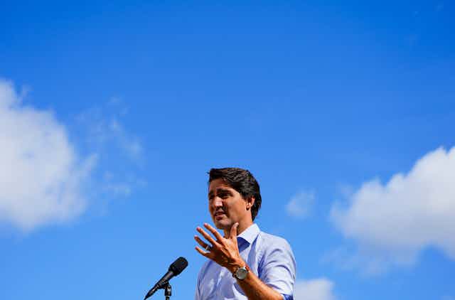 Justin Trudeau standing at a microphone with blue skies behind him