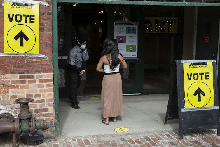 A woman lines up outside a building to vote with yellow vote signs on either side of her.