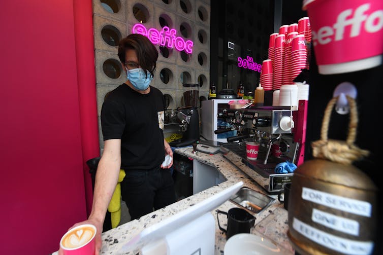Cafe worker in a mask makes coffee.