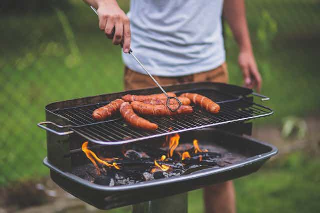 A person grills sausages on a barbecue