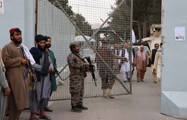 Taliban fighters in Afghan dress and military uniforms guard the gates at Kabul airport.