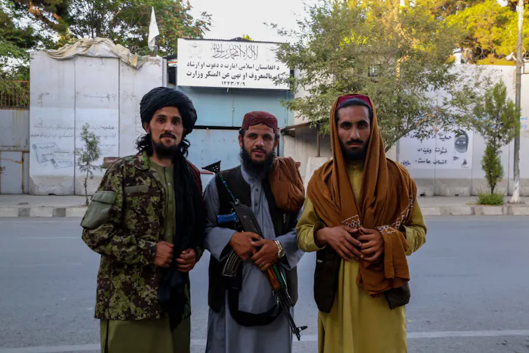 Three Taliban fighters stand outside the former Ministry for Women Affairs which has a new sigh stating it is the Ministry of Vice and Virtue.