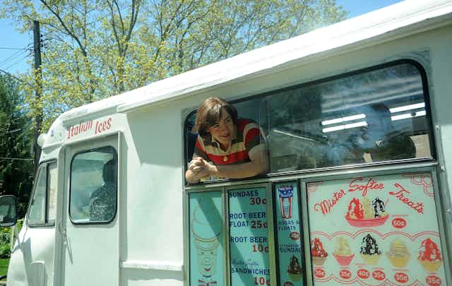 Young man leans out the window of an ice cream truck.