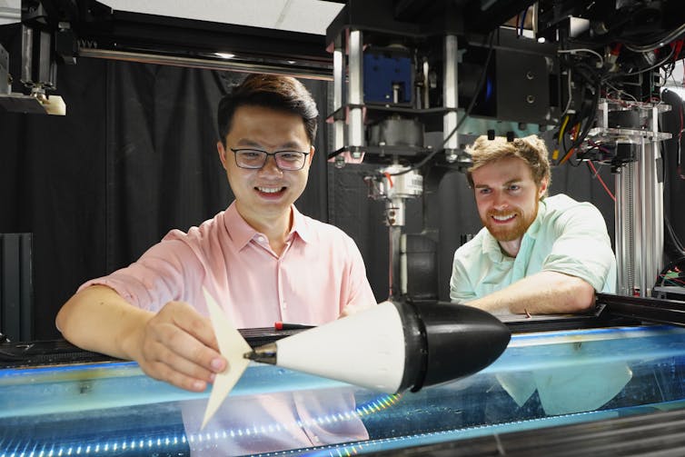 Two people standing with a fish robot over a tank of water.