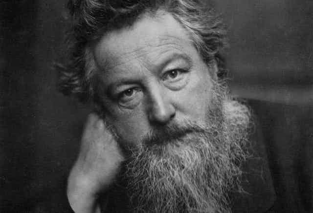 Black and white photo of William Morris with greying beard leaning his head on his hand.