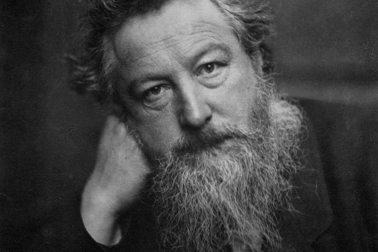 Black and white photo of William Morris with greying beard leaning his head on his hand.