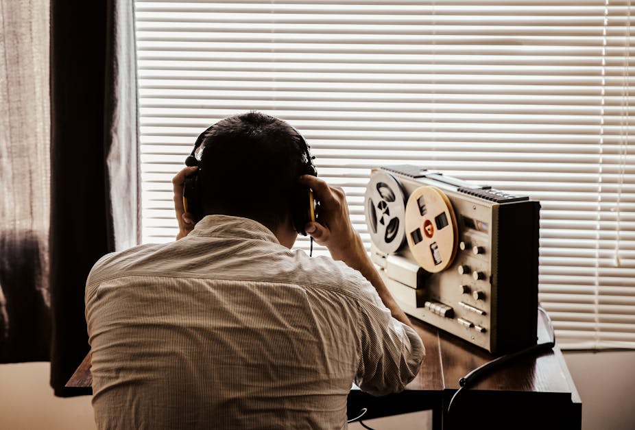 A man wearing headphones listens to conversation on a reel tape recorder