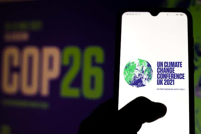 A hand holding a phone with the COP26 logo on it.