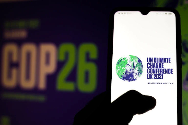 A hand holding a phone with the COP26 logo on it.