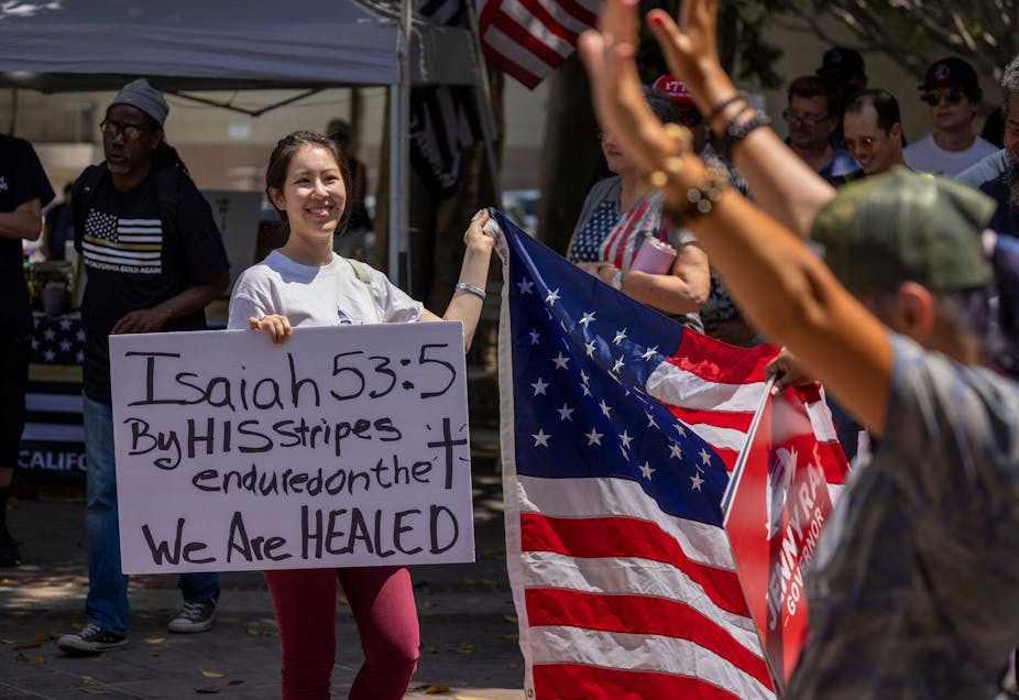 A woman holds a sign quoting Isaiah 53:5 in the Bible as anti-vaccination protesters pray and gather near City Hall in Los Angeles.